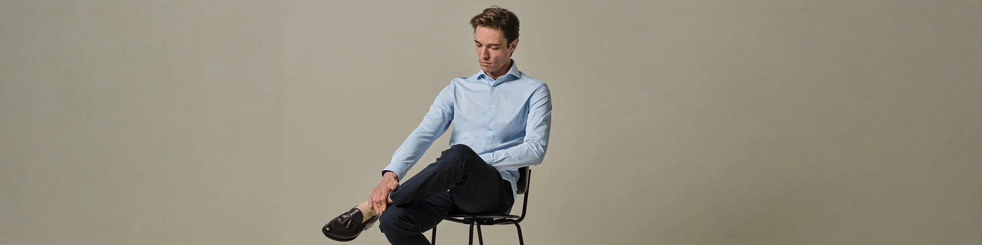 Man in lichtblauw Profuomo Japanese Knitted overhemd op stoel, gecombineerd met donkere chino en bruine tassel loafers