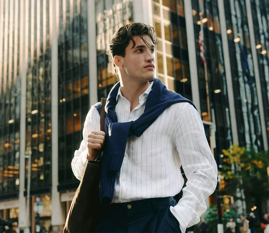 Man in wit gestreept overhemd met trui nonchalant over de schouders in old money stijl