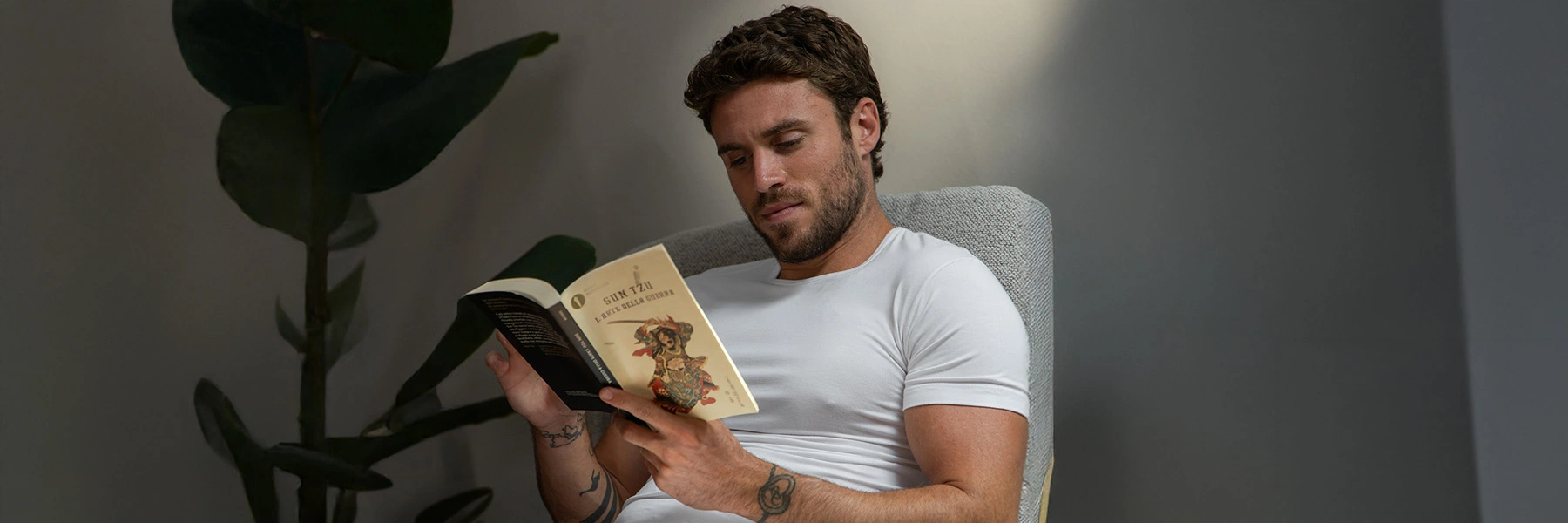 Man draagt extra lang wit T-shirt voor heren terwijl hij ontspannen een boek leest.