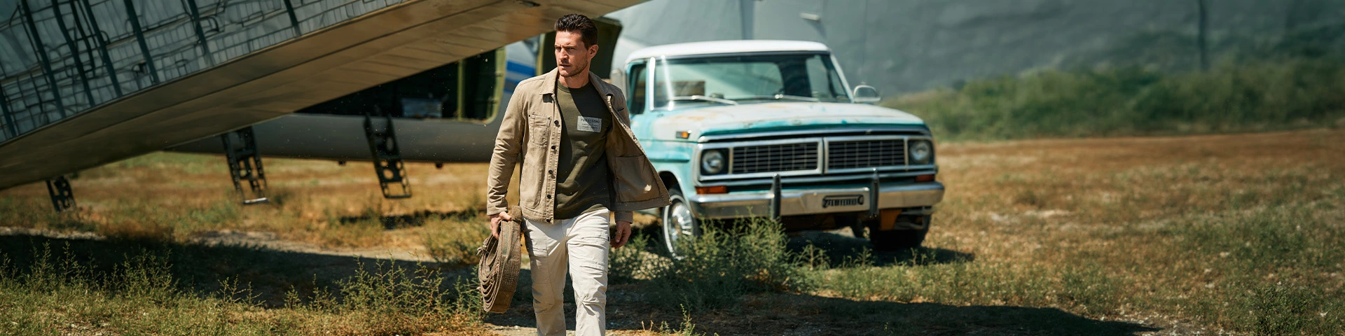 Model draagt een stijlvolle casual outfit met overshirt en lichte broek bij een vintage pick-uptruck.