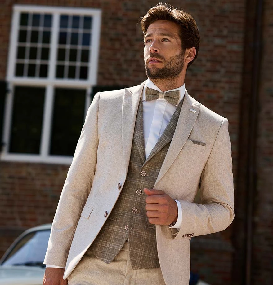 Bruidegom in licht beige trouwpak met gilet en vlinderdas, geschikt voor een zomerse bruiloft